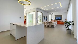Une cuisine moderne dotée d’un îlot central, un coin repas avec une table ronde et des chaises, et un espace de vie avec un canapé et un téléviseur.