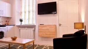 Ein kompakter Wohnbereich mit Küchenzeile, einem an der Wand befestigten Fernseher, einer Couch und einem Tisch mit einer Schüssel darauf.