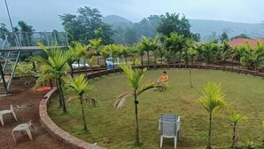 A grassy area with small palm trees and a few plastic chairs. - Niwant Resort (Mahad)
