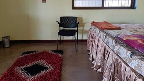 A room with a bed, a chair, a window, and a patterned rug. - Niwant Resort (Mahad)
