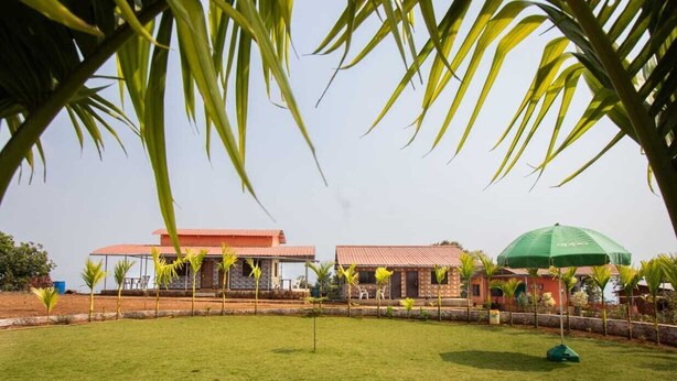 A building with a red roof and a green umbrella in the foreground. - Niwant Resort (Mahad)
