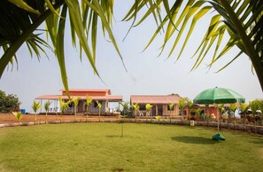 A building with a red roof and a green umbrella in the foreground. - Niwant Resort (Mahad)