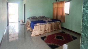 A room with a bed, a ceiling fan, a window with curtains, and a tiled floor. - Niwant Resort (Mahad)