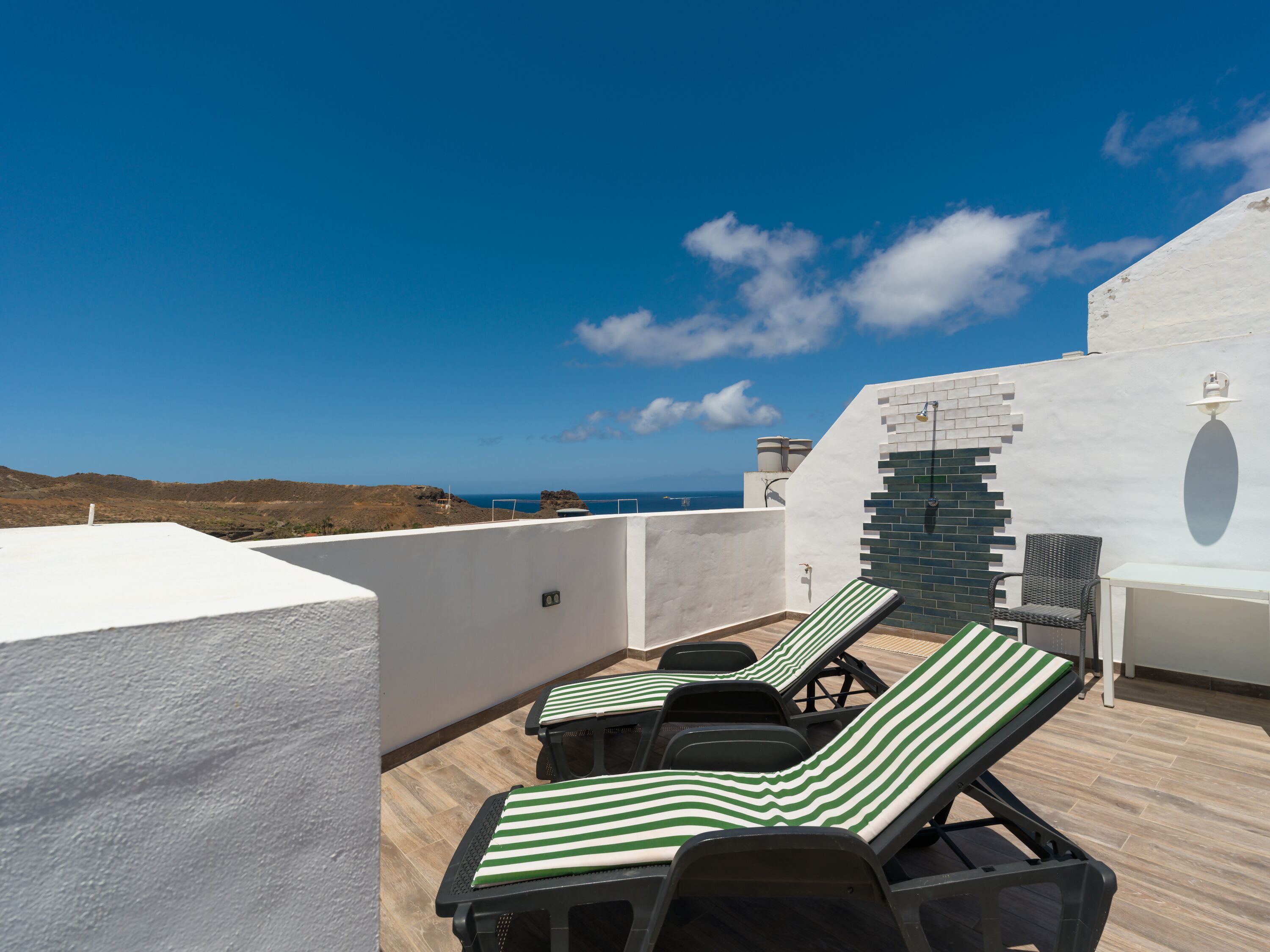 A rooftop terrace with two lounge chairs, a small table, and a view of the ocean.