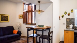 Un espacio habitable compacto con una mesa de comedor, sillas, un sofá, un ventilador y una zona de cocina con estufa y platos decorativos.