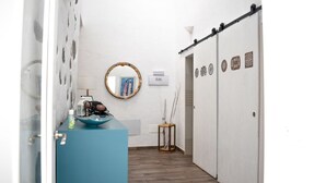 Un pasillo estrecho con una barra azul, un espejo redondo y una puerta con paneles decorativos.