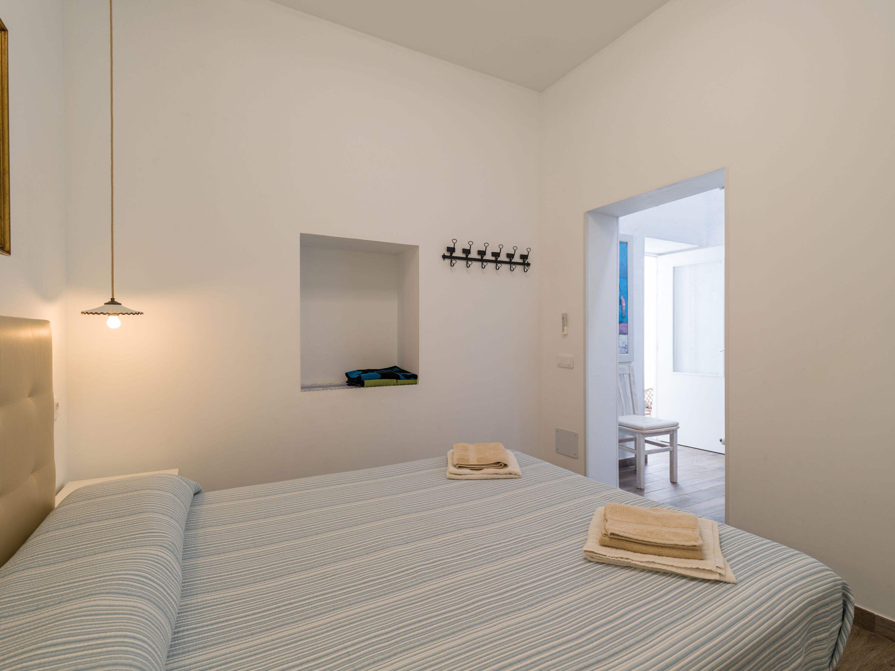 A bedroom with a bed, a hanging light fixture, a coat rack, and a door leading to another room.