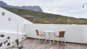 Un balcon avec deux fauteuils en osier et une petite table, donnant sur un paysage montagneux.