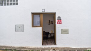 Un bâtiment blanc avec une porte donnant sur une pièce. Il y a une fenêtre au-dessus de la porte, une petite table avec une lampe à l’intérieur et un panneau avec la lettre « W » sur le mur.