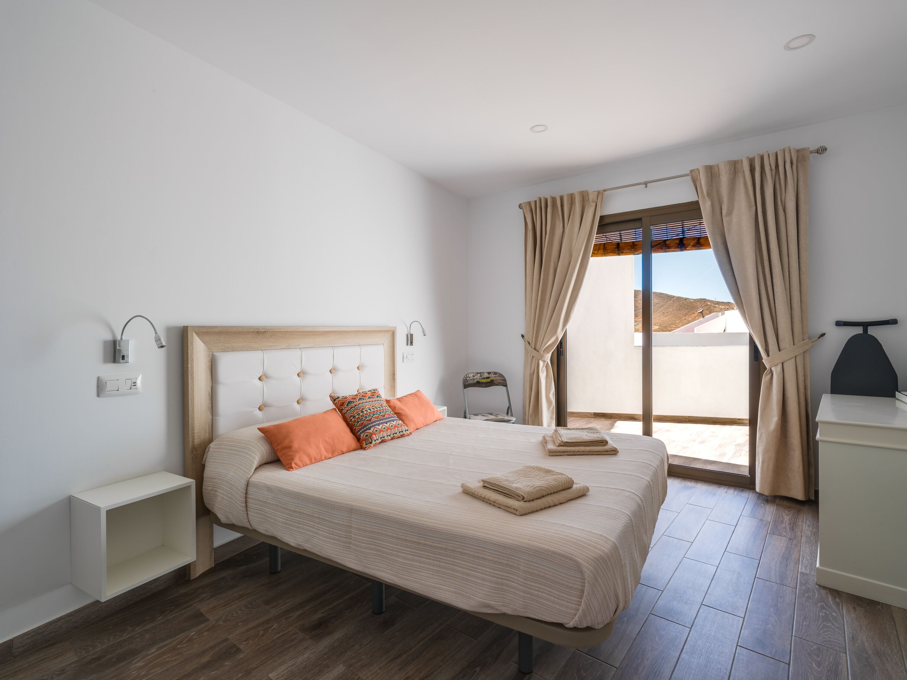 Une chambre à coucher comprenant un lit, des tables de chevet, une commode, une fenêtre avec des rideaux et une vue sur l’extérieur.
