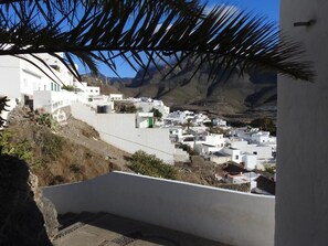 A coastal village with white buildings, a palm tree, and mountains in the background.