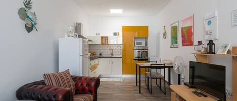 Un espacio habitable compacto con kitchenette, un sofá, una mesa de comedor y un televisor.