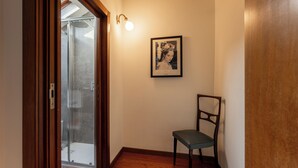 A hallway with a wooden floor, a framed picture on the wall, and a chair. - Castello Sforzesco, Lieux Caches Undermyname (Milano)