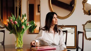 A woman sitting at a wooden table with a vase of tulips, a pink notebook, and a cup. - Castello Sforzesco, Lieux Caches Undermyname (Milano)