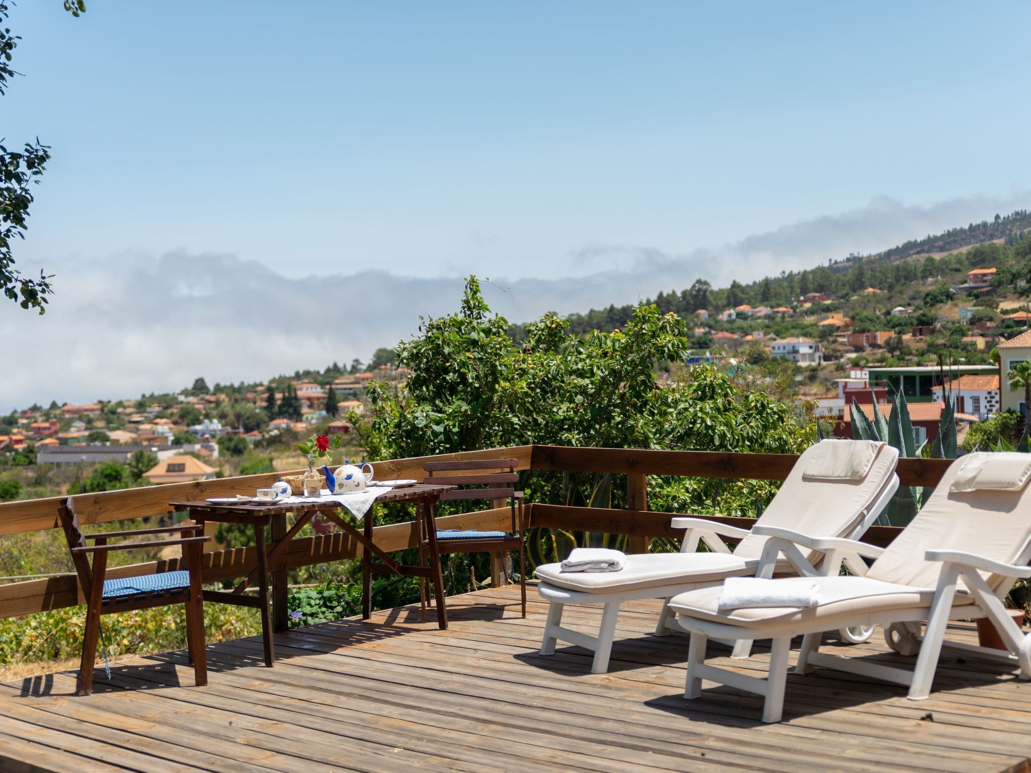 A wooden deck with a table, chairs, and lounge chairs overlooking a mountainous landscape.