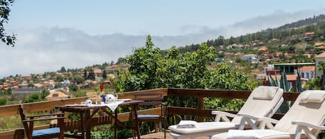 A wooden deck with a table, chairs, and lounge chairs overlooking a mountainous landscape.