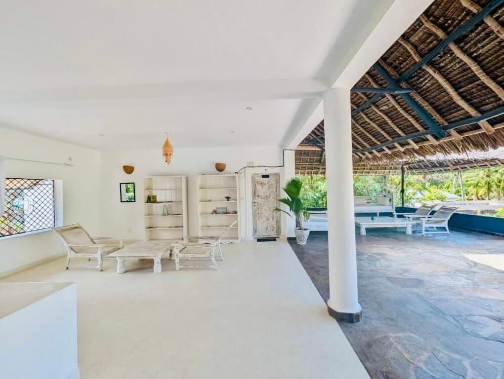 A spacious indoor area with a high ceiling, a thatched roof structure, and a seating area with chairs and a table.