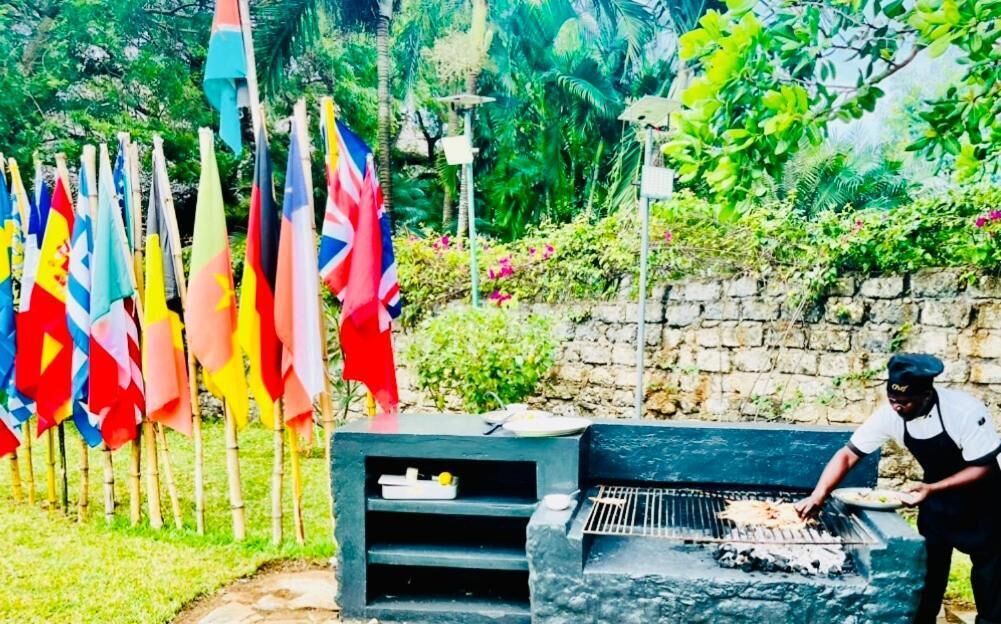 A person grilling outdoors with a stone barbecue and flags in the background.