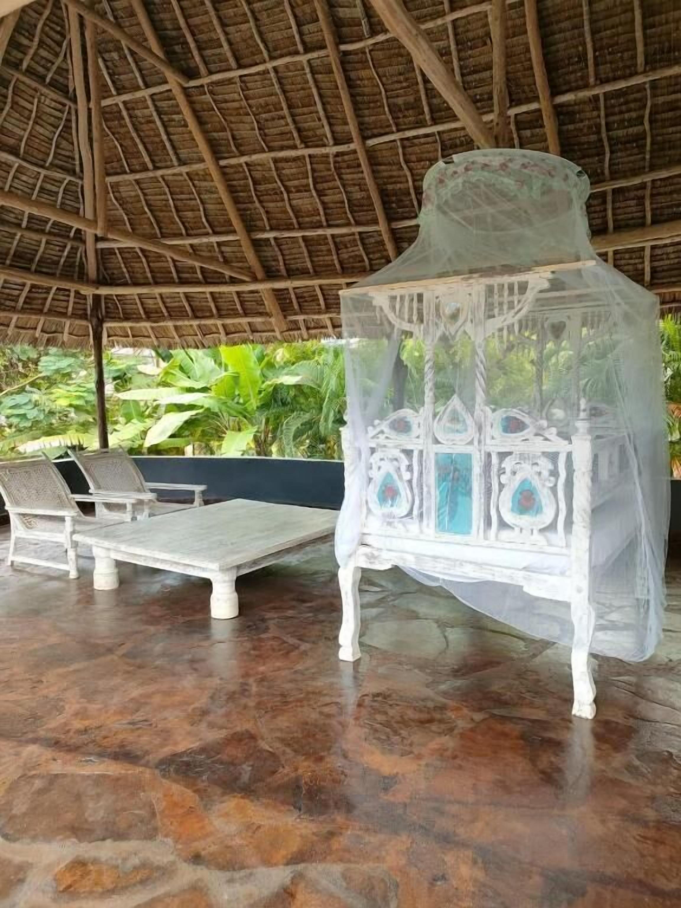 A covered outdoor seating area with a thatched roof, white cushioned chairs, and a decorative white chair with a canopy.
