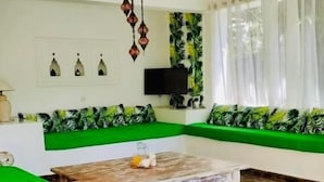 Uma sala de estar com um sofá verde, uma mesa de centro de madeira e um chão com padrão de pedra.