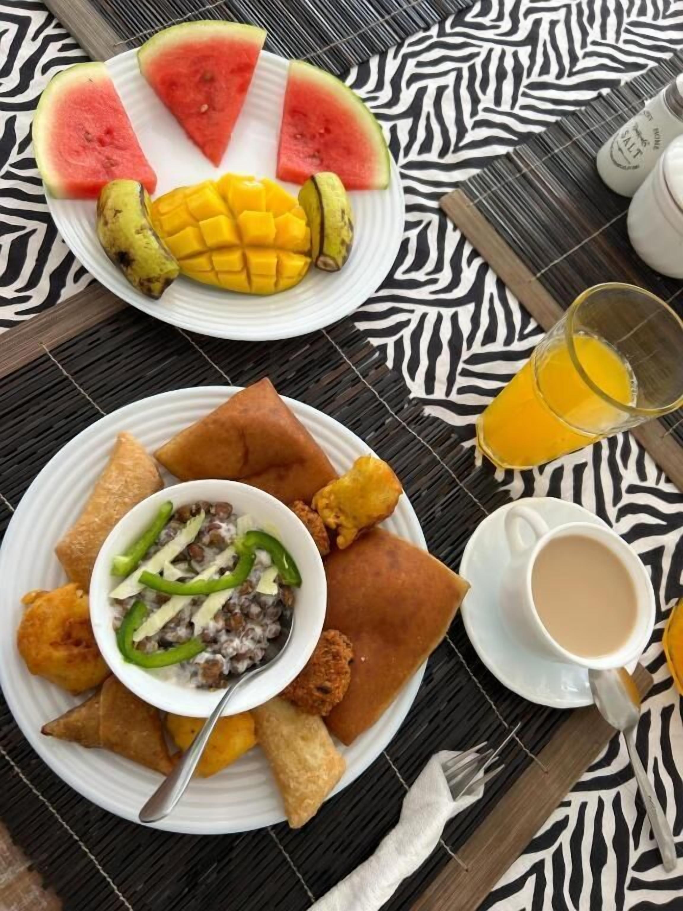 A table with a plate of food including watermelon, mango, and fried items, a bowl of salad, and a cup of coffee.