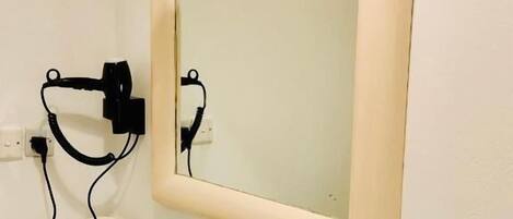Une salle de bain avec un lavabo blanc, un miroir, un porte-serviettes, une petite plante et un luminaire.