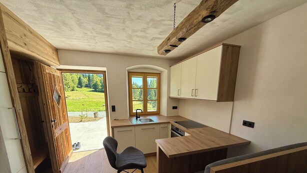 Eine kleine Küche mit Holdekor-Schränken, einer eingebauten Spüle und einem Fenster mit Blick auf eine grüne Landschaft.