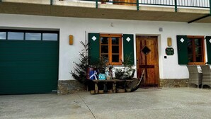 Ein Gebäude mit grüner Garagentür, einer Holztür und einem kleinen Außenbereich mit Korbsesseln und einem Tisch.
