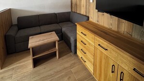 Ein modernes Wohnzimmer mit einem Ecksofa, einer Holzkommode, einem wandmontierten Flachbildfernseher und einem Couchtisch aus Holz.