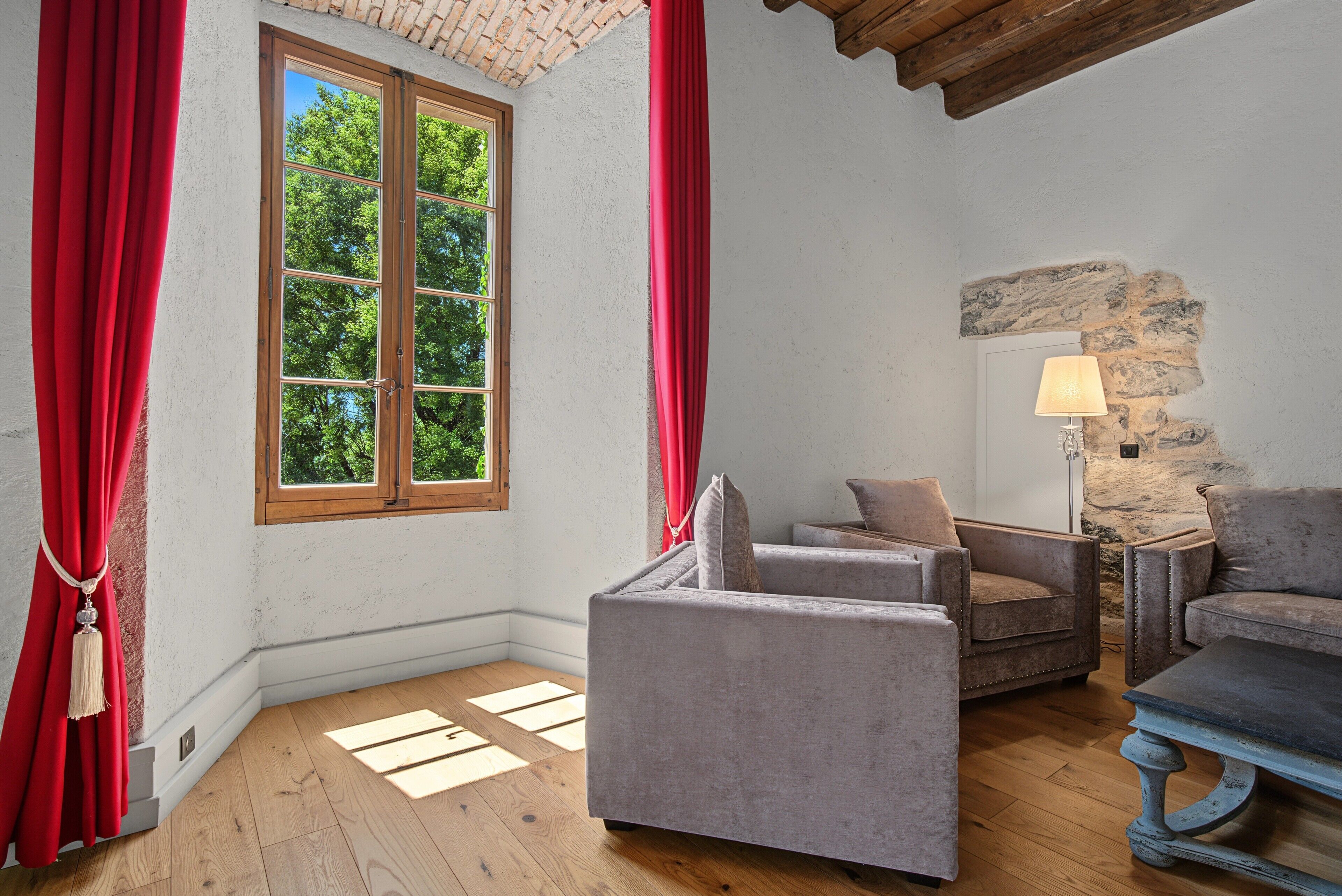 Une pièce avec une grande fenêtre, un mur en pierre, une lampe et deux fauteuils.