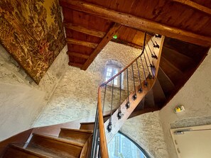 Un escalier en bois avec une rampe, des murs en pierre et une fenêtre en haut.