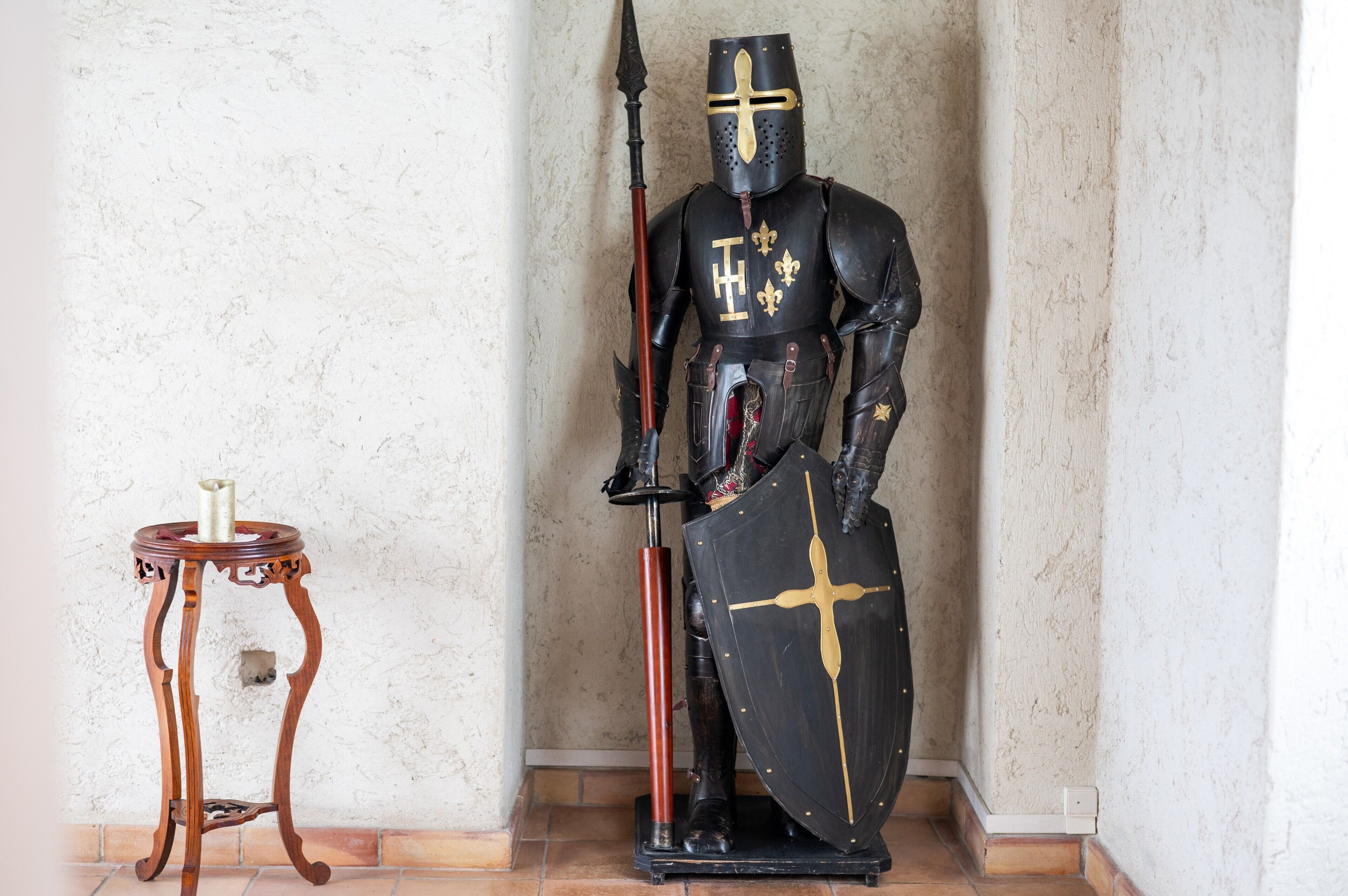 Une statue d’un chevalier médiéval, revêtu d’une armure et tenant un bouclier, se dresse à côté d ’une table en bois sur laquelle est posée une bougie.