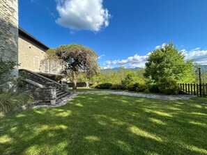 Un bâtiment en pierre avec un escalier menant à une porte, entouré d’une pelouse bien entretenue et d’arbres.
