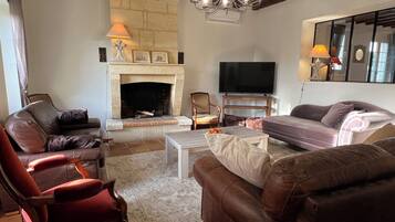 A living room with a fireplace, leather sofas, a television, and a chandelier.