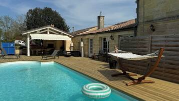 A swimming pool with a wooden deck, a hammock, and outdoor furniture.