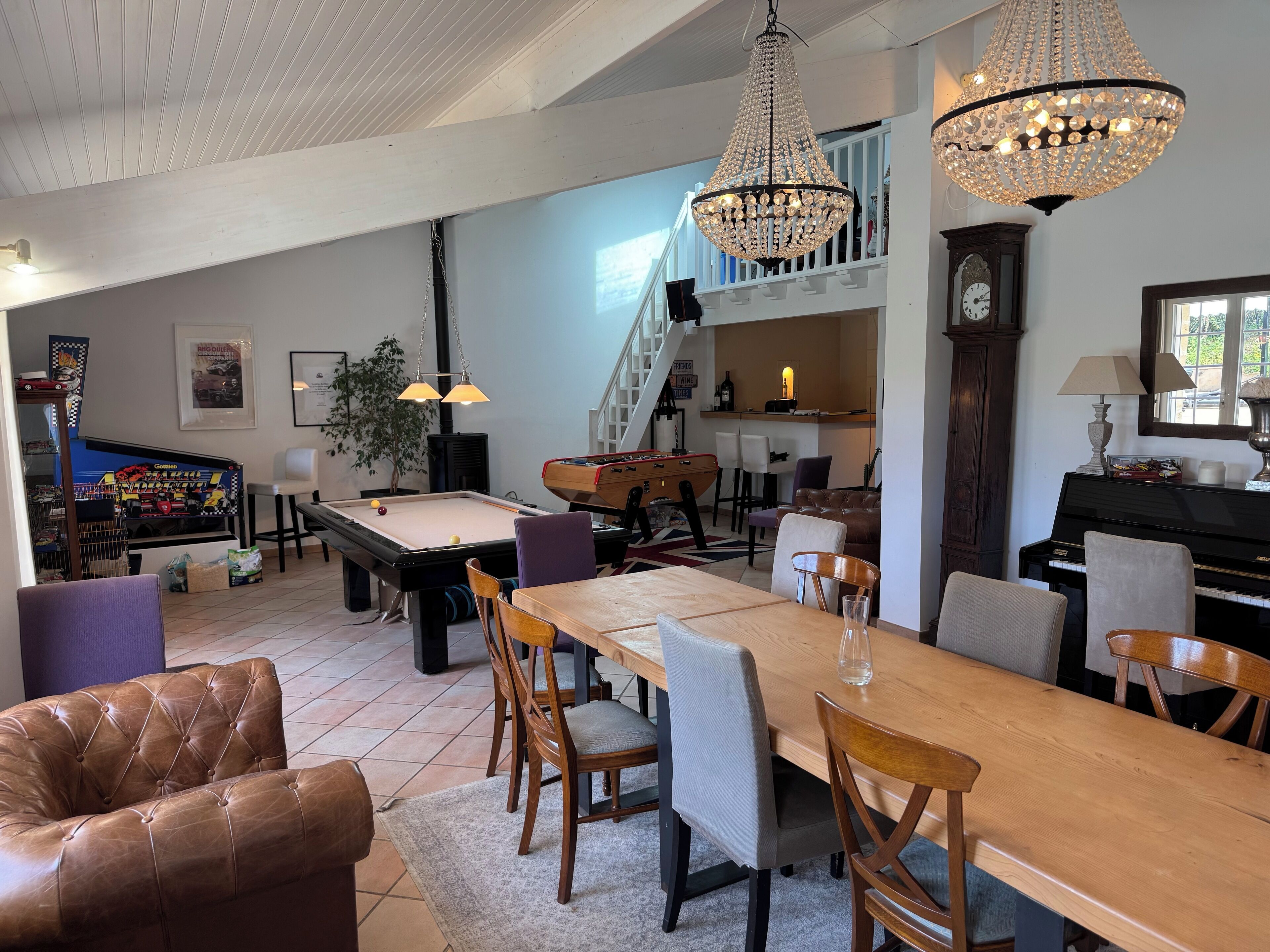 Un vaste espace de vie comprenant une table de billard, un canapé en cuir, une table à manger et deux lustres.