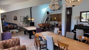 A spacious living area with a pool table, leather sofa, dining table, and two chandeliers.
