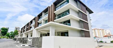 Un edificio residencial moderno de varios pisos, con balcones, techo plano y entrada protegida por un portón.