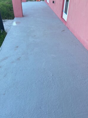 Een betonnen pad dat naar een gebouw leidt, met een roze gevel en een raam.