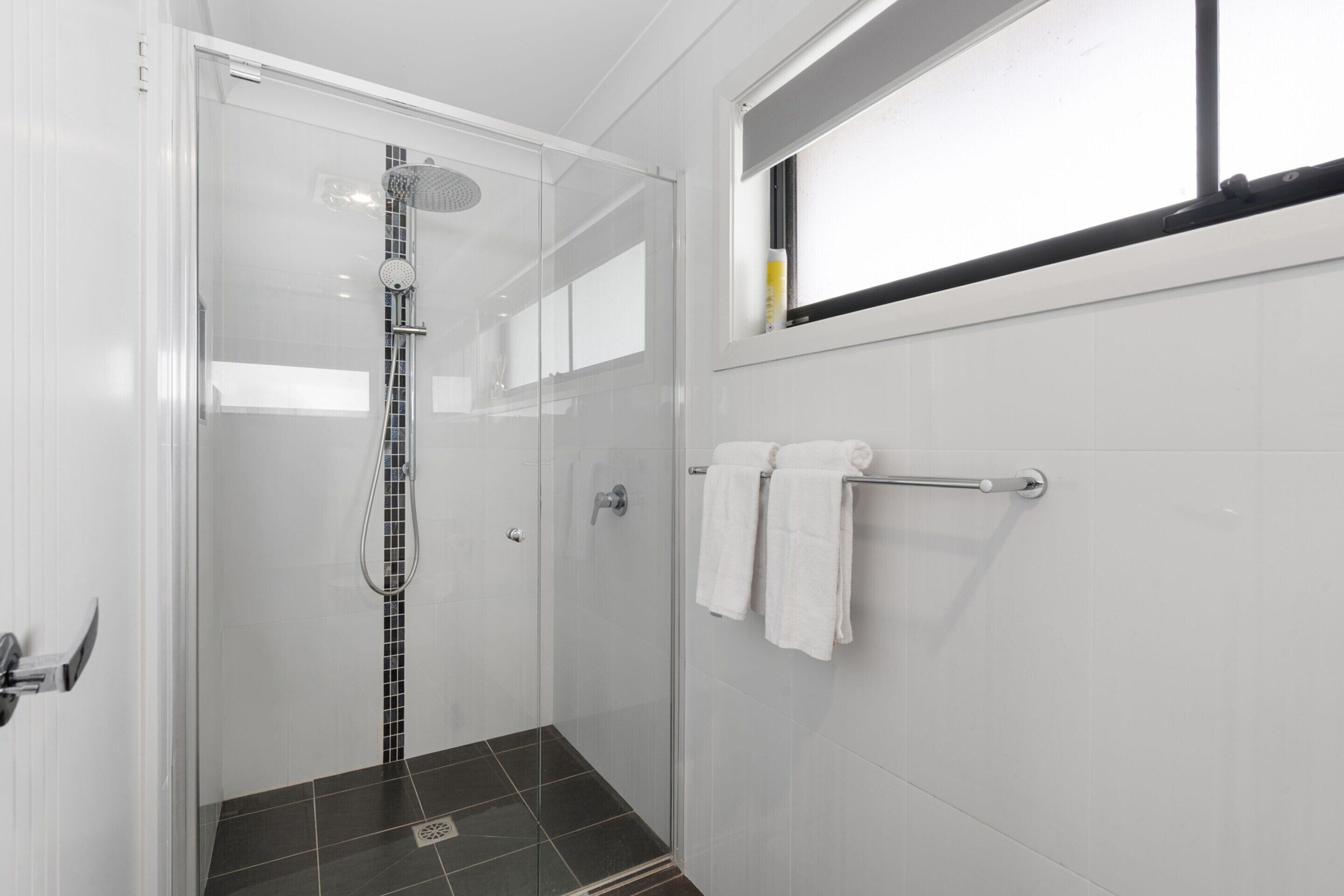 A modern bathroom with a glass shower enclosure, a towel rack, and a window.