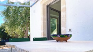 A table with a colorful bowl, green chairs, and a white wall with a window. - Recently renovated Lamia, surrounded by olive trees and Mediterranean vegetation (Ostuni)