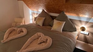 Een net opgemaakt bed met hoofdbord, kussens en een bedlampje.