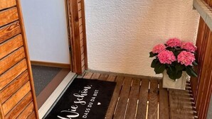 Een houten deur met een zwarte deurmat waarop staat: 'Wie schön, dass du bist'.