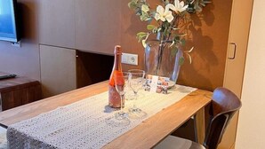 Een eettafel met een fles en glazen, een bloemenvaas en een televisie aan de muur.