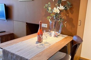 A dining table with a bottle and glasses, a vase with flowers, and a television on the wall. - Seegold | Seenah | seeglueck (Konstanz)
