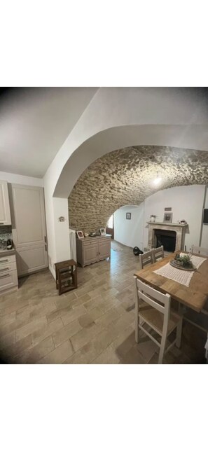 Een ruime keuken met een stenen boog, een houten eettafel en witte kasten.