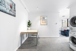 A modern, well-lit room with a dining area, a potted plant, a painting, and a washing machine. - Bright Inner-city Stay Near Roma Street (Brisbane)