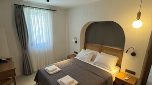 Une chambre d’hôtel bien rangée, avec un lit, des tables de chevet, un bureau et une fenêtre avec des rideaux.