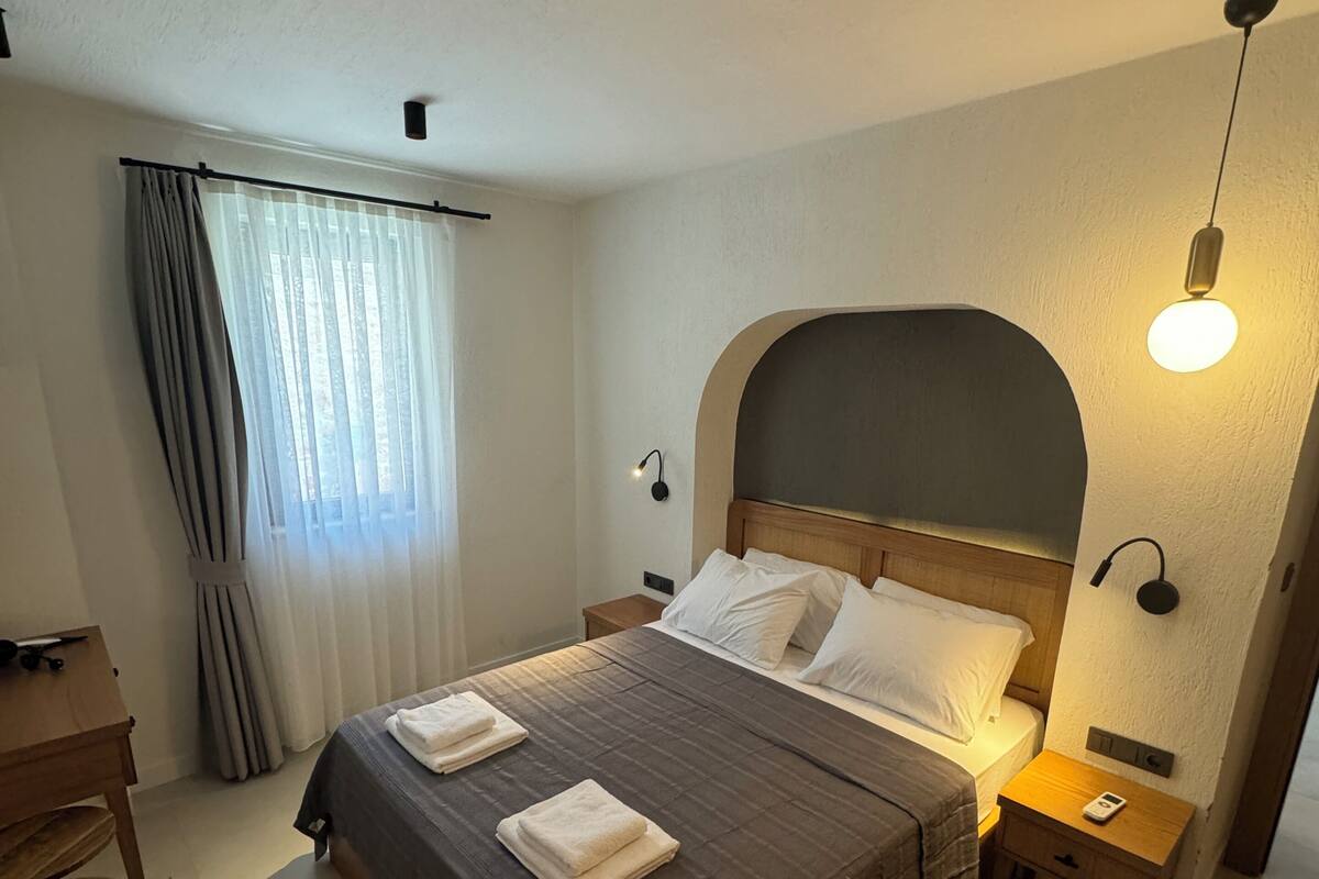 A neatly arranged hotel room with a bed, bedside tables, a desk, and a window with curtains.