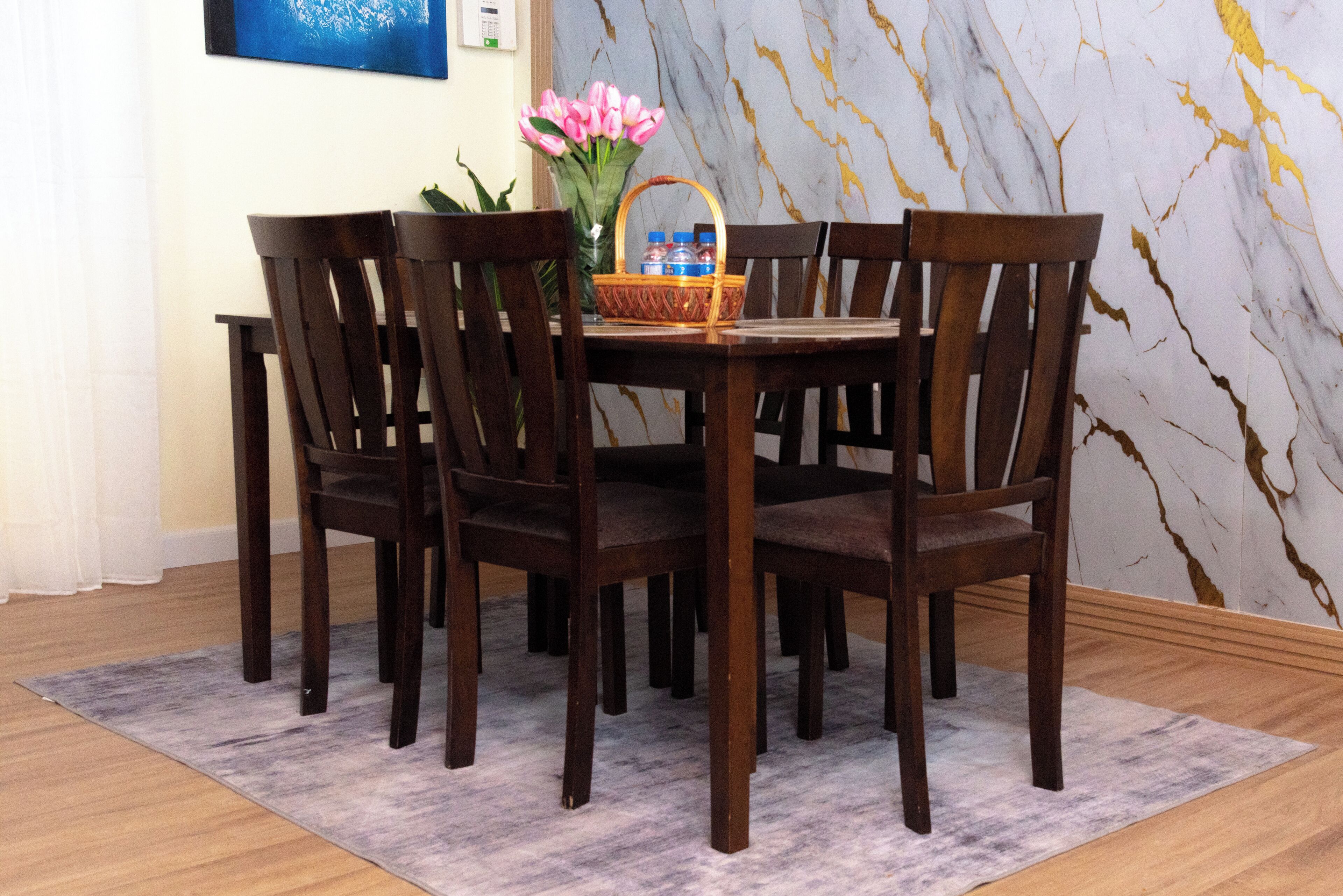 A dining area with a marble wall, wooden chairs, a table, and a vase with flowers.